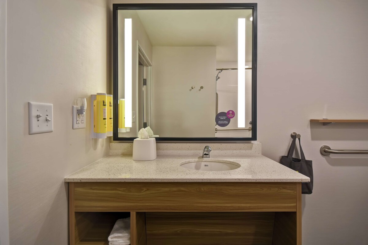 Une salle de bain avec un grand miroir, un lavabo, un porte-serviettes et une étagère contenant des articles de toilette.