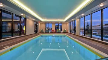 Una piscina interior con paredes de vidrio transparente, suelo de baldosas y vistas al exterior.
