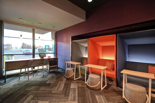 Een moderne kantoorruimte met een groot raam, een bureau met stoelen en een zithoek met een bank en voetenbankje.