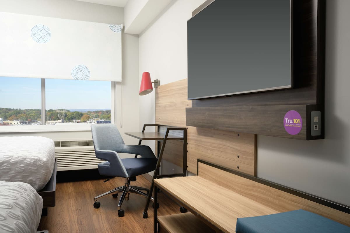 Una camera d'albergo con un letto, una scrivania, una sedia, una televisione e una finestra vista sulla città.