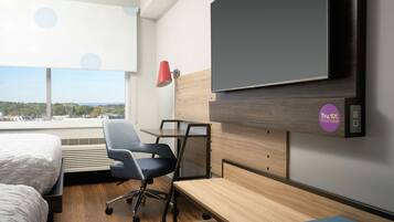 Una camera d'albergo con un letto, una scrivania, una sedia, una televisione e una finestra vista sulla città.