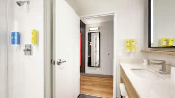 A modern bathroom with a glass shower enclosure, a white sink with a speckled countertop, and a mirror above the sink.