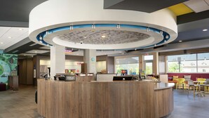 A modern reception area with a central wooden counter, a circular ceiling design, and a seating area with yellow chairs. - Tru By Hilton Chattanooga Hamilton Place (Chattanooga)