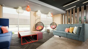 A modern lounge area with a blue sofa, a red coffee table, and two hanging chairs with cushions. - Tru By Hilton Chattanooga Hamilton Place (Chattanooga)