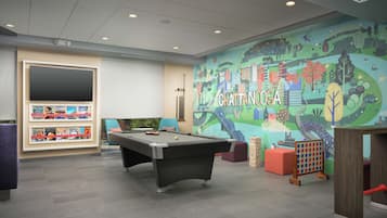 Una mesa de billar en una habitación con un mural de Chattanooga, una estantería con revistas y una zona de estar con sillas.