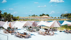 A beachside outdoor seating area with tables and chairs under large umbrellas, overlooking a body of water and a distant shoreline. - Holiday Inn Changsha Dawangshan by IHG (Changsha)