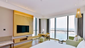 A modern hotel room with a large bed, a desk, a chair, a TV mounted on the wall, and a view of the city through large windows. - Holiday Inn Changsha Dawangshan by IHG (Changsha)
