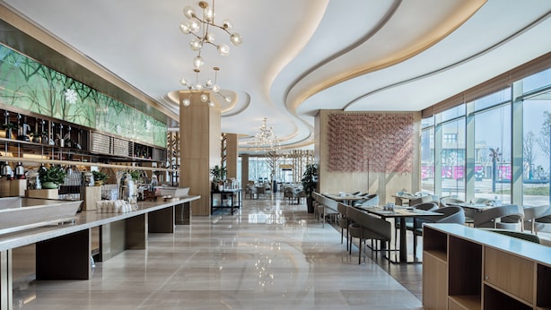 A modern restaurant with a long counter, multiple seating areas, and a large window offering a view of the outside. - Holiday Inn Changsha Dawangshan by IHG (Changsha)