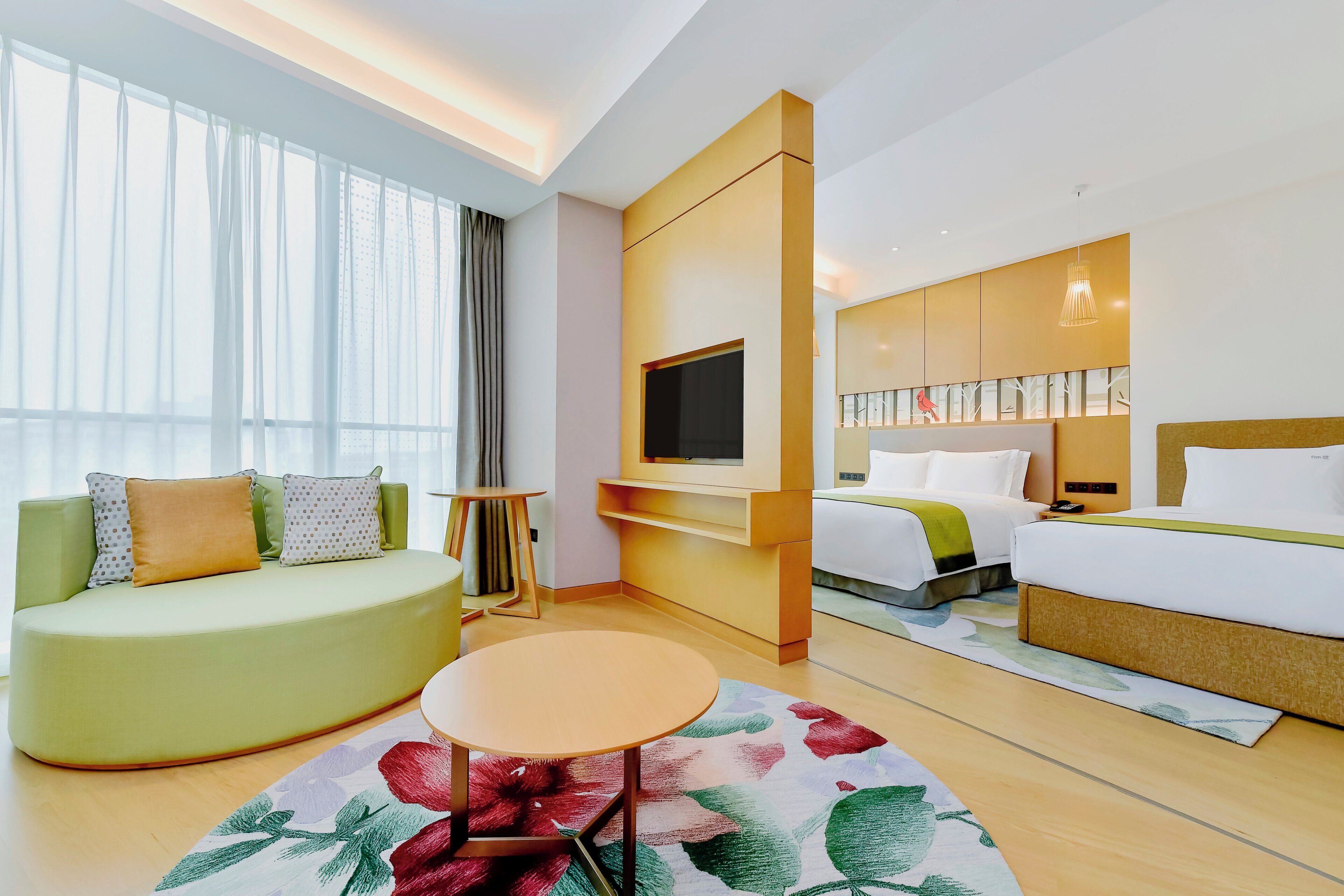 Una habitación de hotel con sofá, cama, televisor montado en la pared y una mesita.