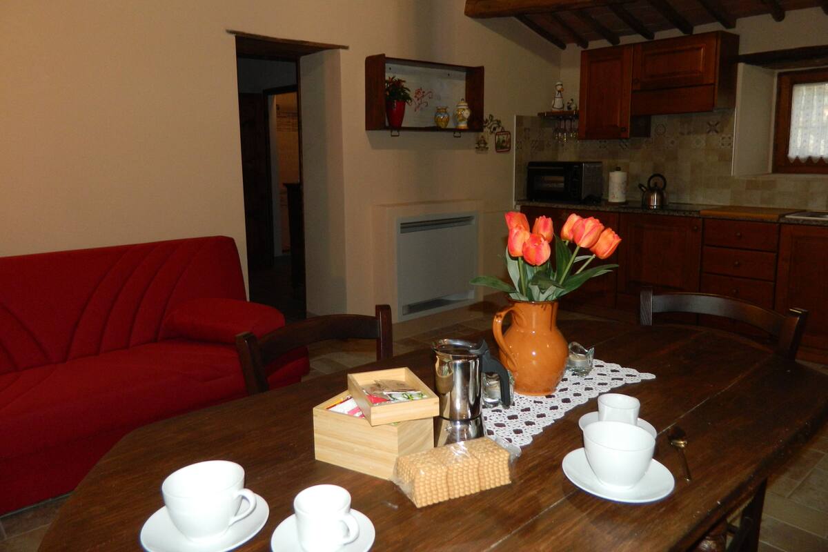 A dining table with a vase of tulips, a teapot, cups, and a box of tea bags.