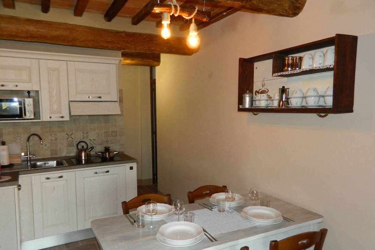A kitchen with white cabinets, a microwave, and a dining table set for four with plates, glasses, and cutlery.
