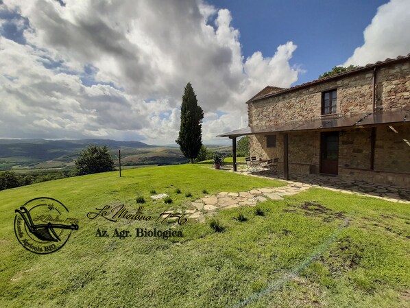 A stone building with a grassy yard and a view of rolling hills.
