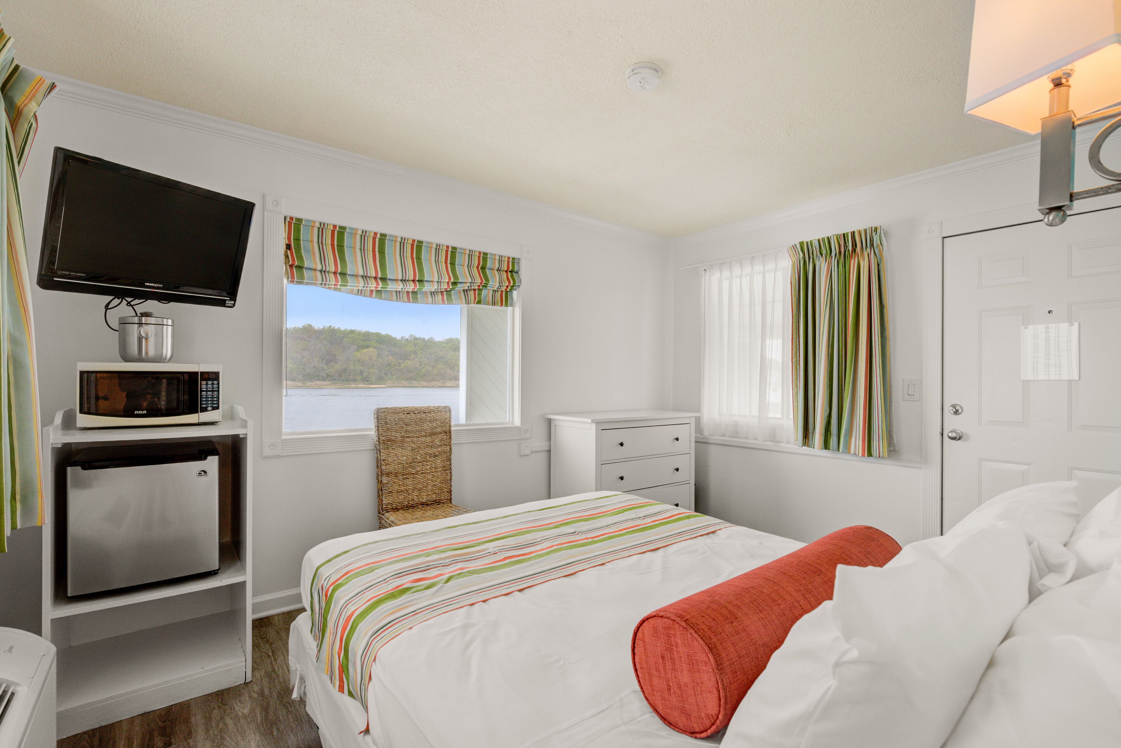 A bedroom with a bed, a television, a microwave, and a window with curtains.