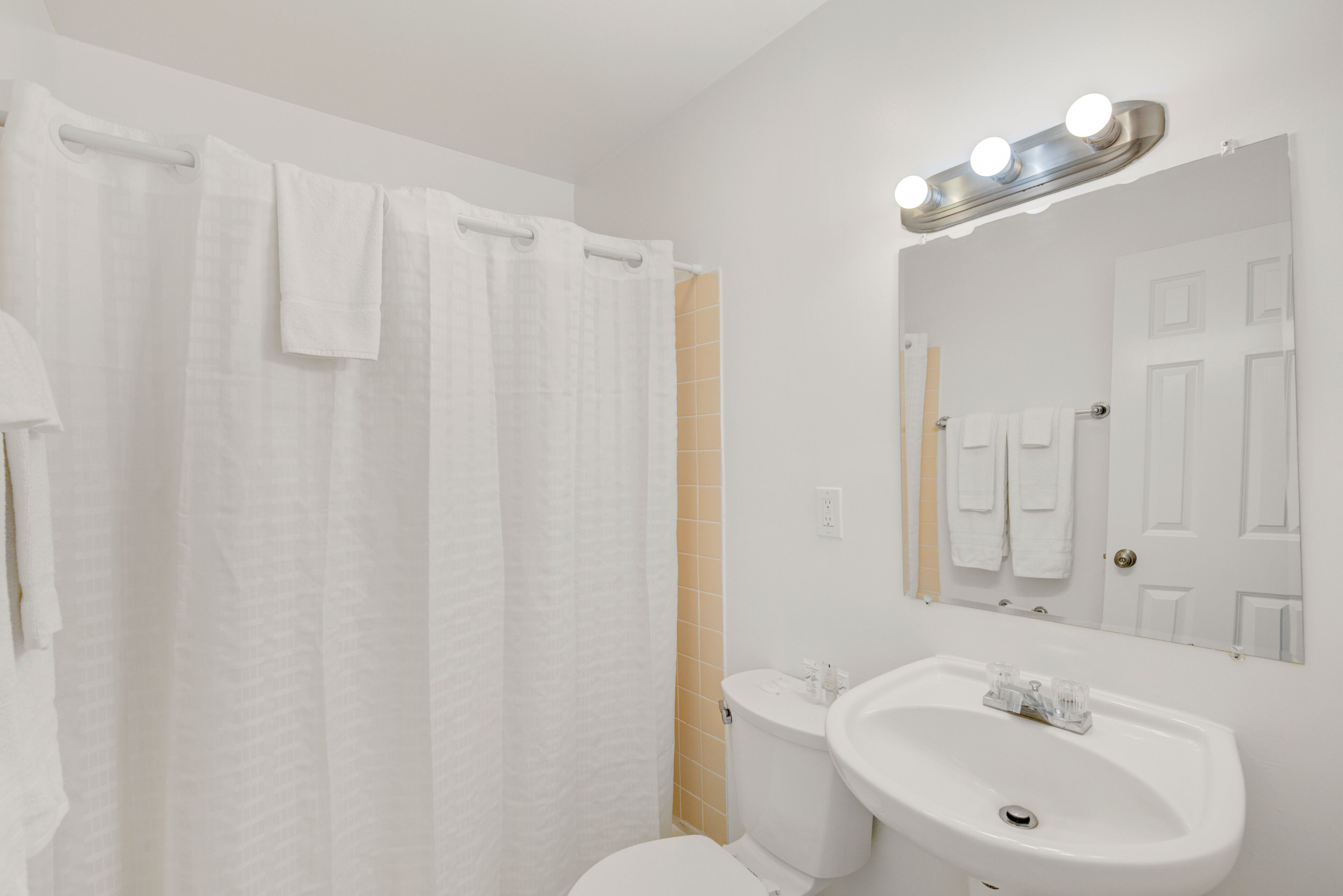 Un baño con inodoro blanco, lavamanos, espejo y cortina de ducha.