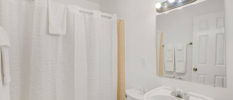 Un baño con inodoro blanco, lavamanos, espejo y cortina de ducha.