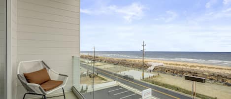 A balcony with a wicker chair, a view of the beach, and a fire lane sign.