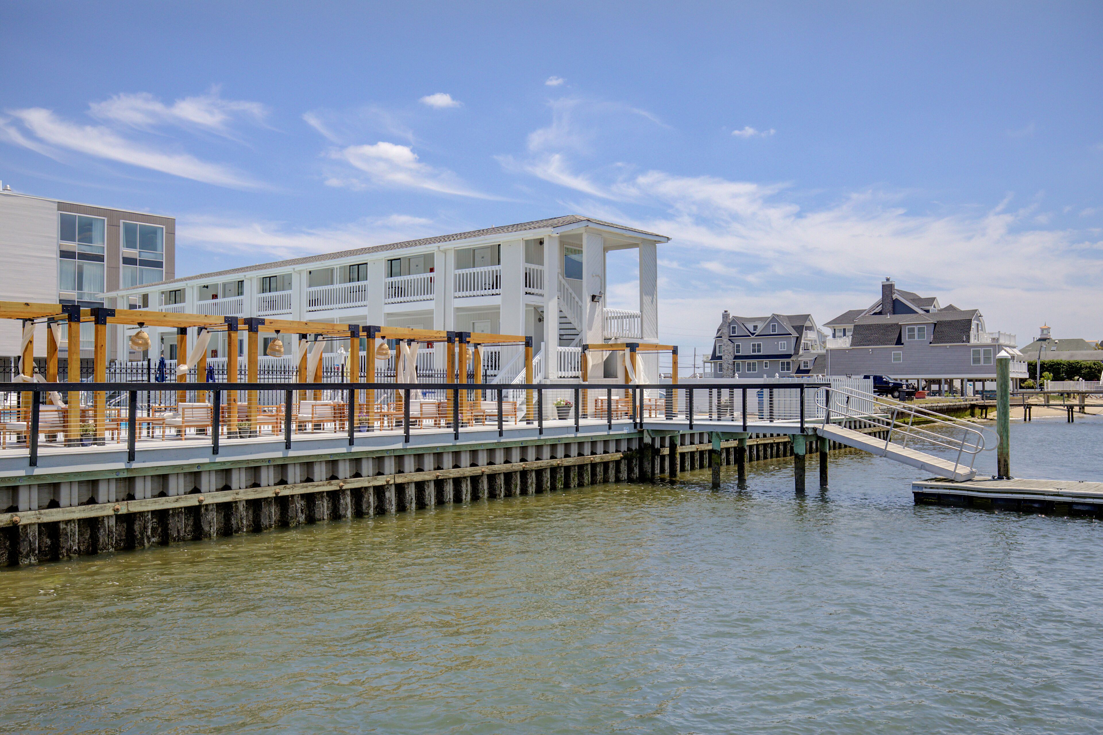 A waterfront property with a wooden deck, white building, and dock extending into the water.