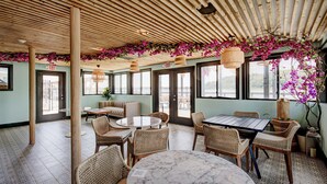 Amplio espacio interior con techo de madera, muebles de mimbre y grandes ventanales que ofrecen vistas al exterior.