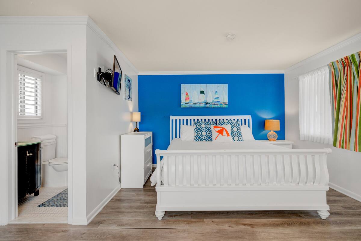 A bedroom with a white bed, a blue accent wall, and a nautical-themed painting.