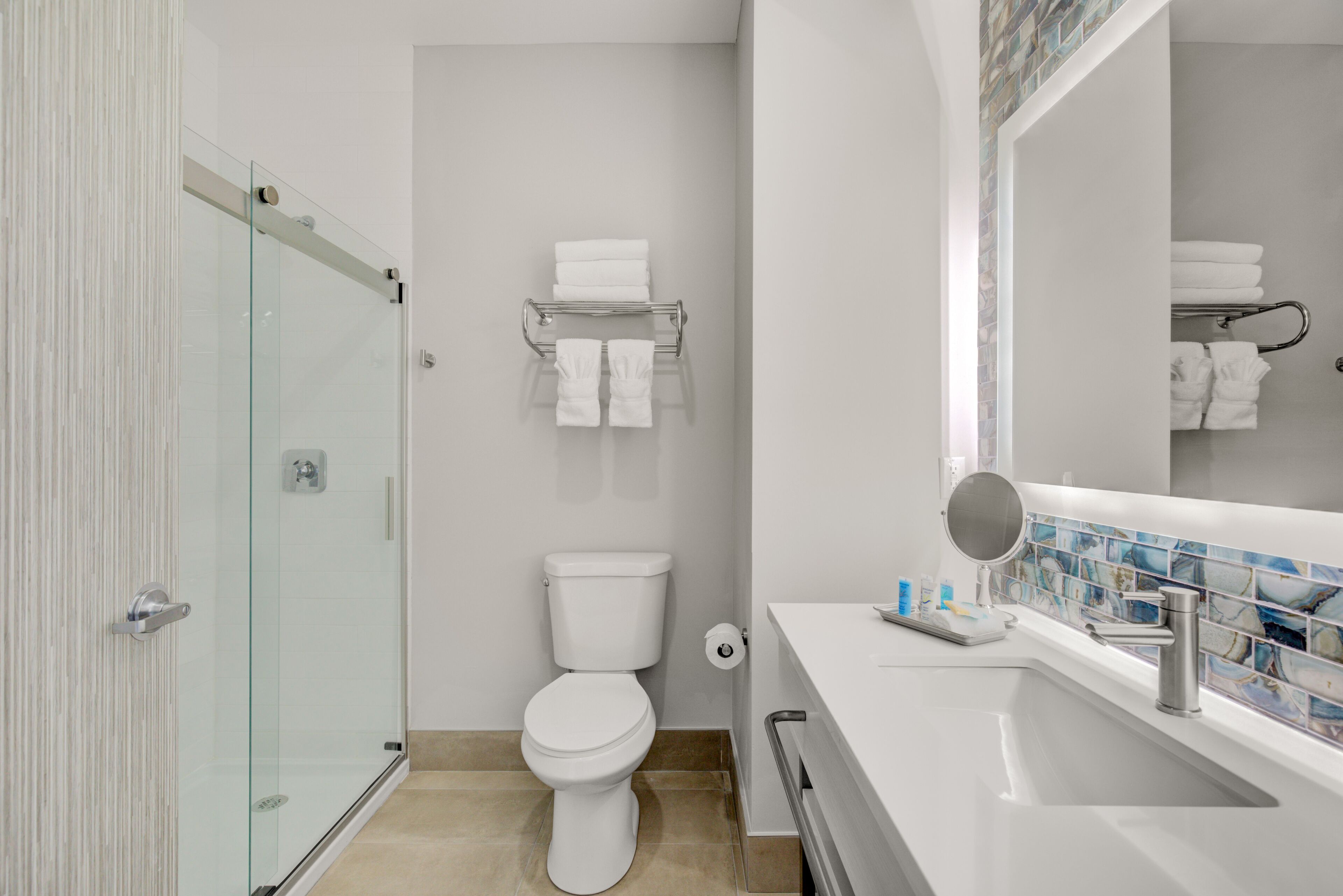 A modern bathroom with a glass shower enclosure, a white toilet, a white sink with a mirror, and a tiled backsplash.