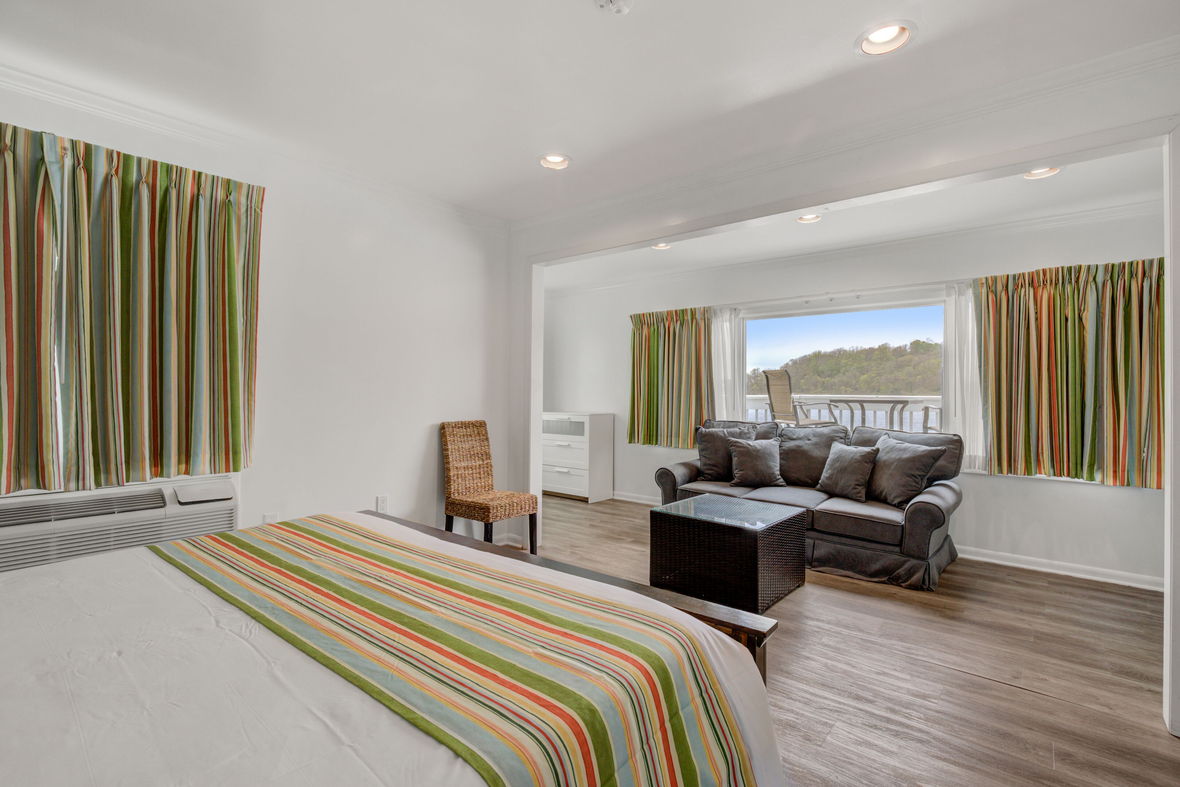 Un'ampia camera da letto con un letto grande, un divano e una poltrona. Alle finestre sono presenti delle tende, e si può ammirare un panorama sull'esterno.