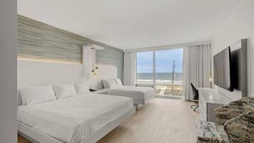 Una habitación de hotel moderna con dos camas, un ventanal con vistas al mar, un televisor de pantalla plana y un escritorio con una silla.