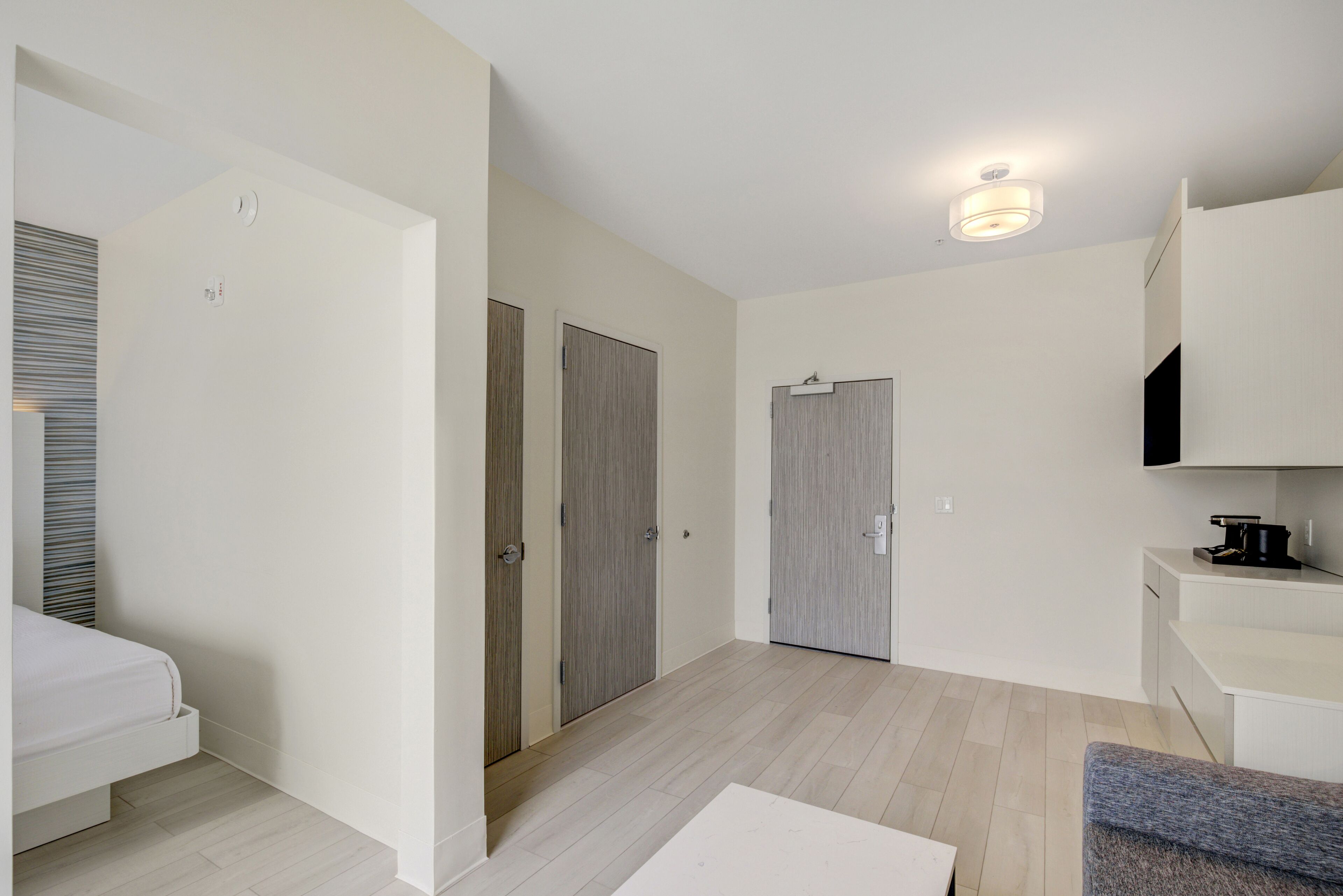 A modern hotel room with a bed, a desk, and a kitchenette.