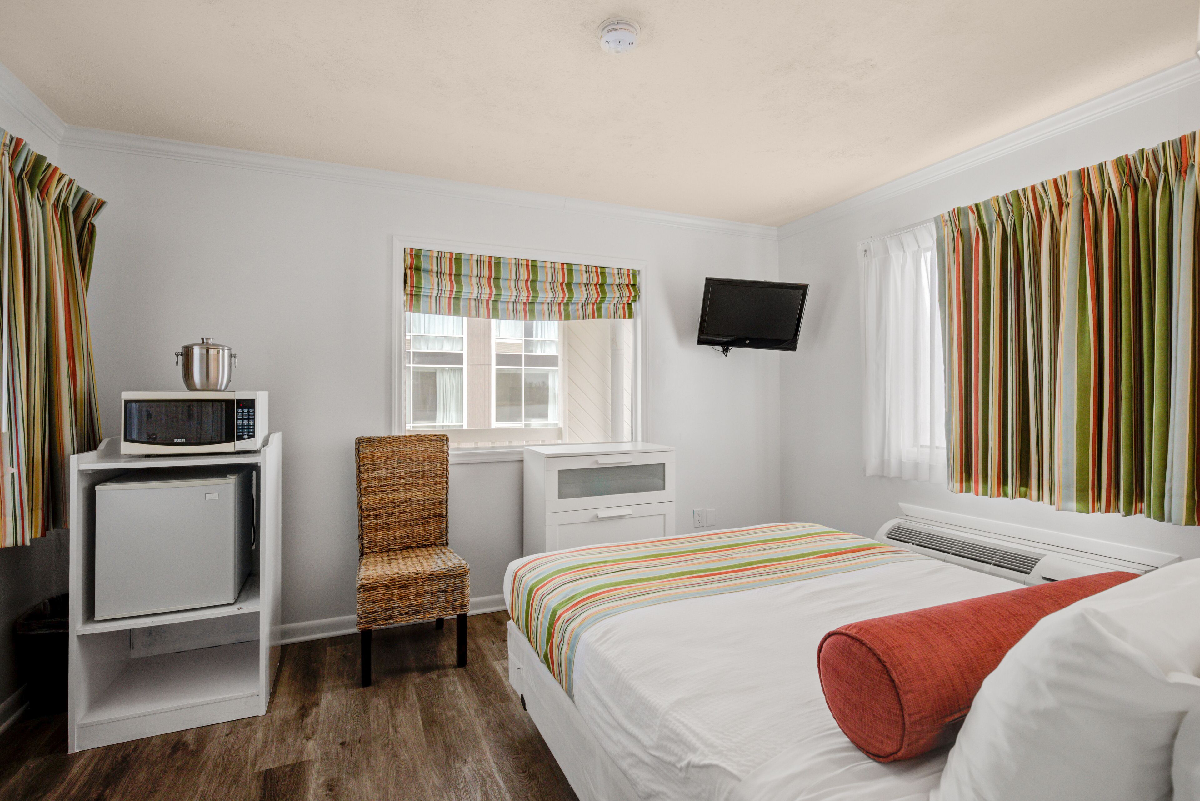 A hotel room with a bed, a chair, a small desk with a microwave, a television, and a window with curtains.