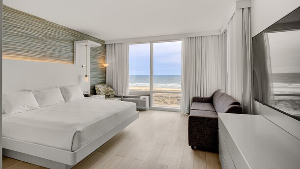 Habitación de hotel moderna con una cama grande, un sofá, una televisión y vistas a la playa.