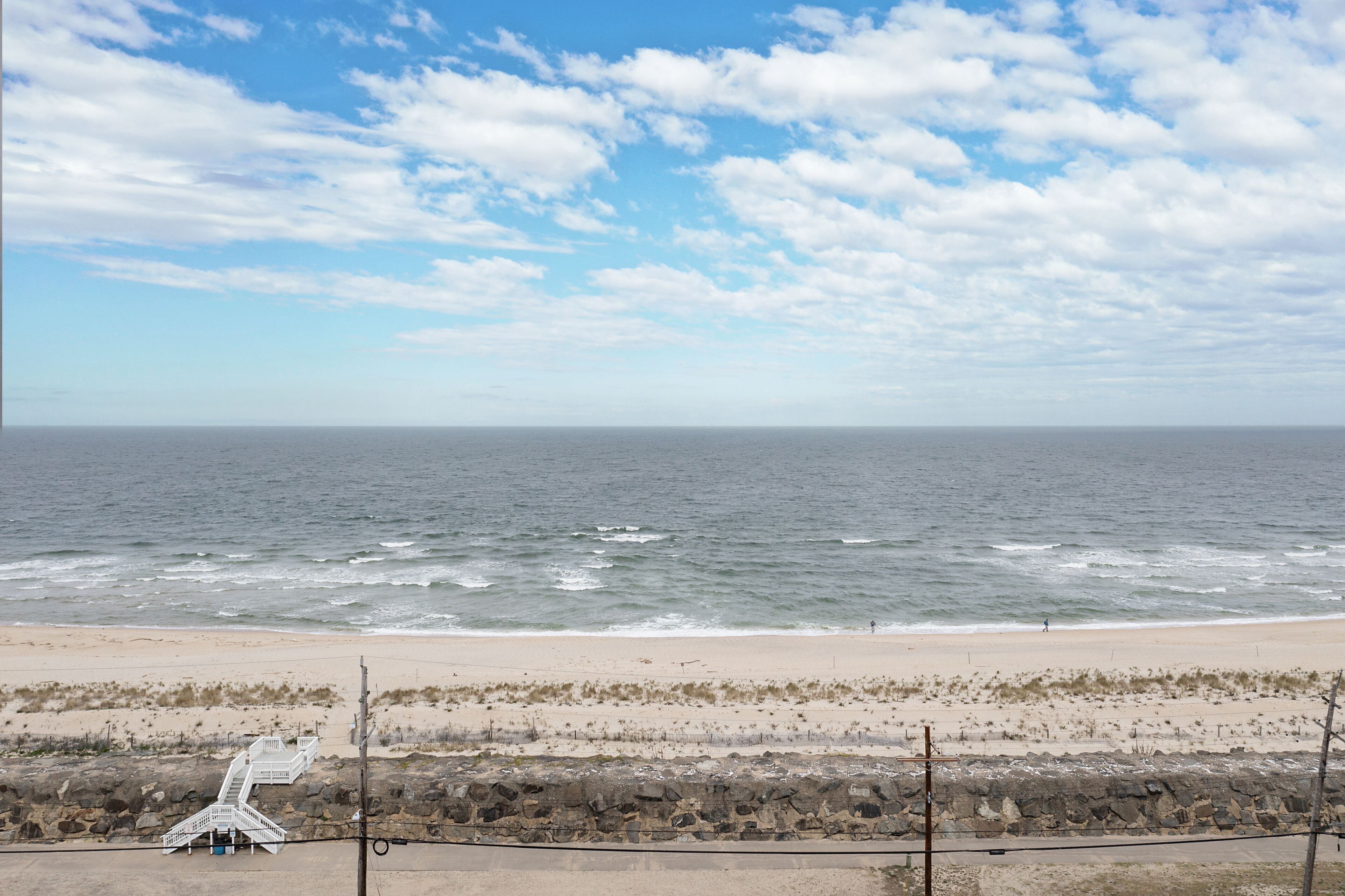 A beach with a rocky shoreline, a staircase leading down to the beach, and the ocean in the background.