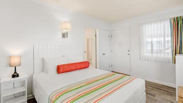 A hotel room with a bed, a nightstand, a lamp, a door, and a window with curtains.