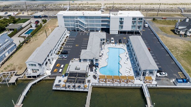 An aerial view of a hotel with a pool, parking area, and a beach view.