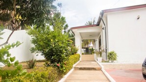 A pathway leading to a white building with a red roof, surrounded by greenery and a parked car. - Sara's place (Tema)