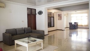 A living room with a grey sofa, a glass coffee table, and a dining area with a table and chairs. - Sara's place (Tema)