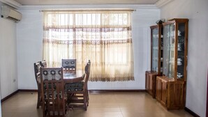 A dining area with a wooden table and chairs, a window with lace curtains, and a wooden cabinet with glass doors. - Sara's place (Tema)