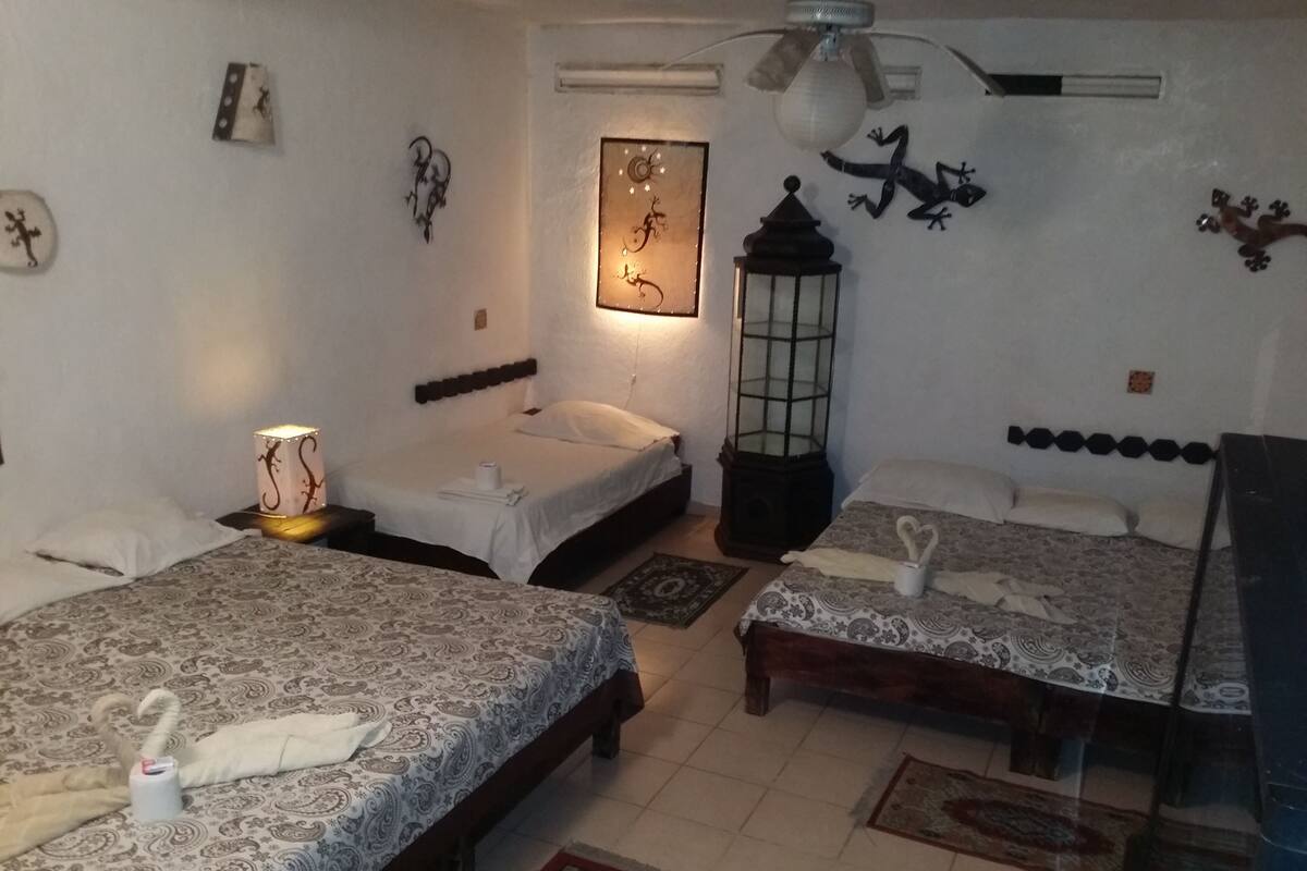 Habitación de hotel con dos camas individuales, una mesita de noche, una lámpara, un calentador de pared, un farol y una pequeña mesa.