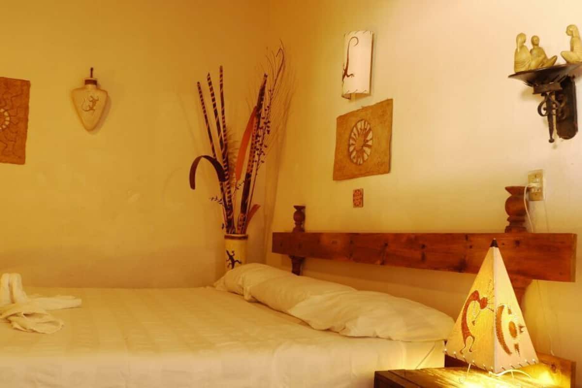 Un dormitorio con cama, mesita de noche, lámpara y adornos en la pared, incluyendo un reloj y una estantería con figuritas.