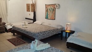 Habitación de hotel con dos camas, una zona de estar con una silla, una mesita pequeña y un adorno en la pared.