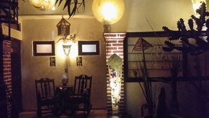 Una habitación tenuemente iluminada con pared de ladrillo, dos cuadros enmarcados, una mesa con sillas y una lámpara colgante.