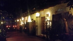 Un sendero tenuemente iluminado que conduce a un edificio con varias ventanas y puertas iluminadas, sugiriendo una entrada acogedora.