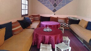 A cozy seating area with a round table, cushioned sofas, and a patterned wall. - Tanssi House (Asni)