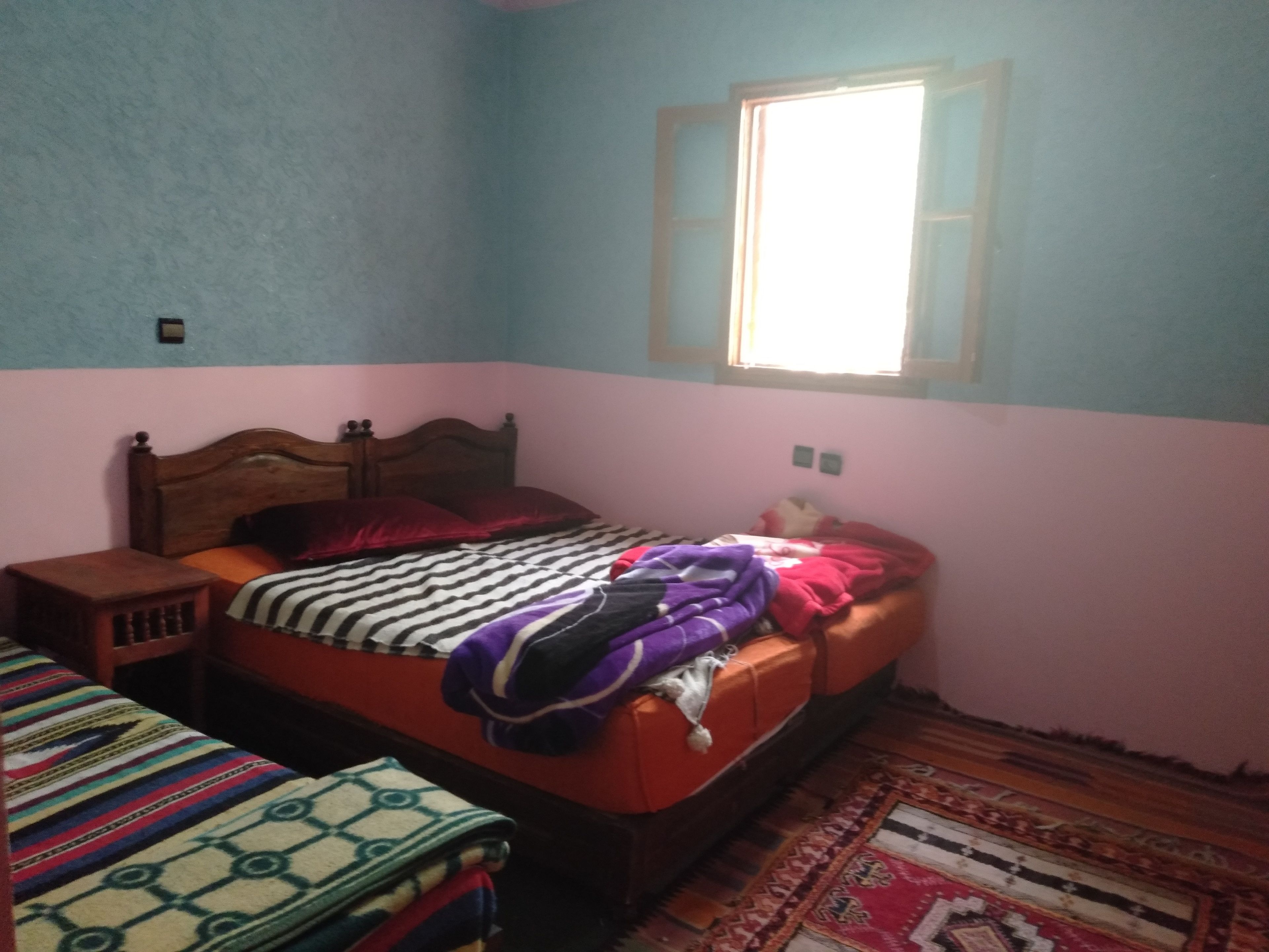 A bedroom with a wooden bed, a nightstand, a window, and a patterned rug.