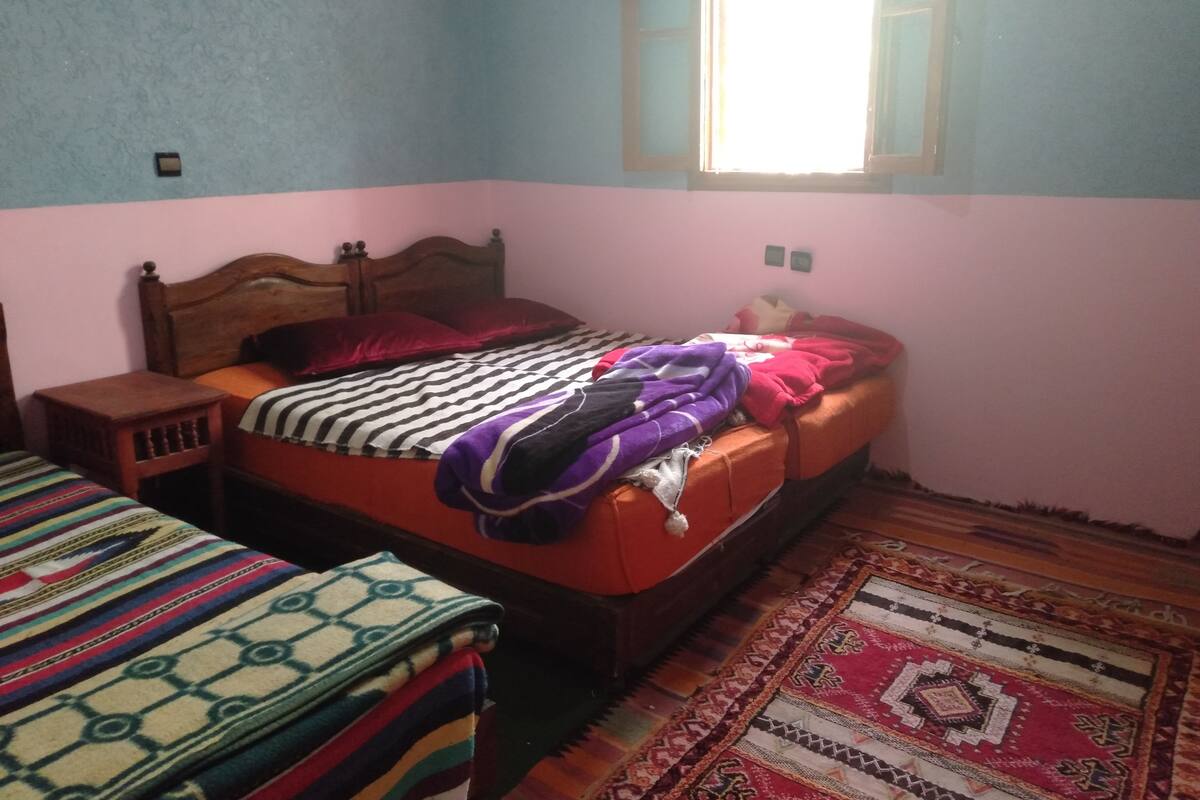 A bedroom with a single bed, a nightstand, a window, and a patterned rug.