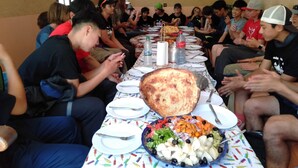 A group of people seated around a table with a large platter of food, plates, and cutlery. - Tanssi House (Asni)