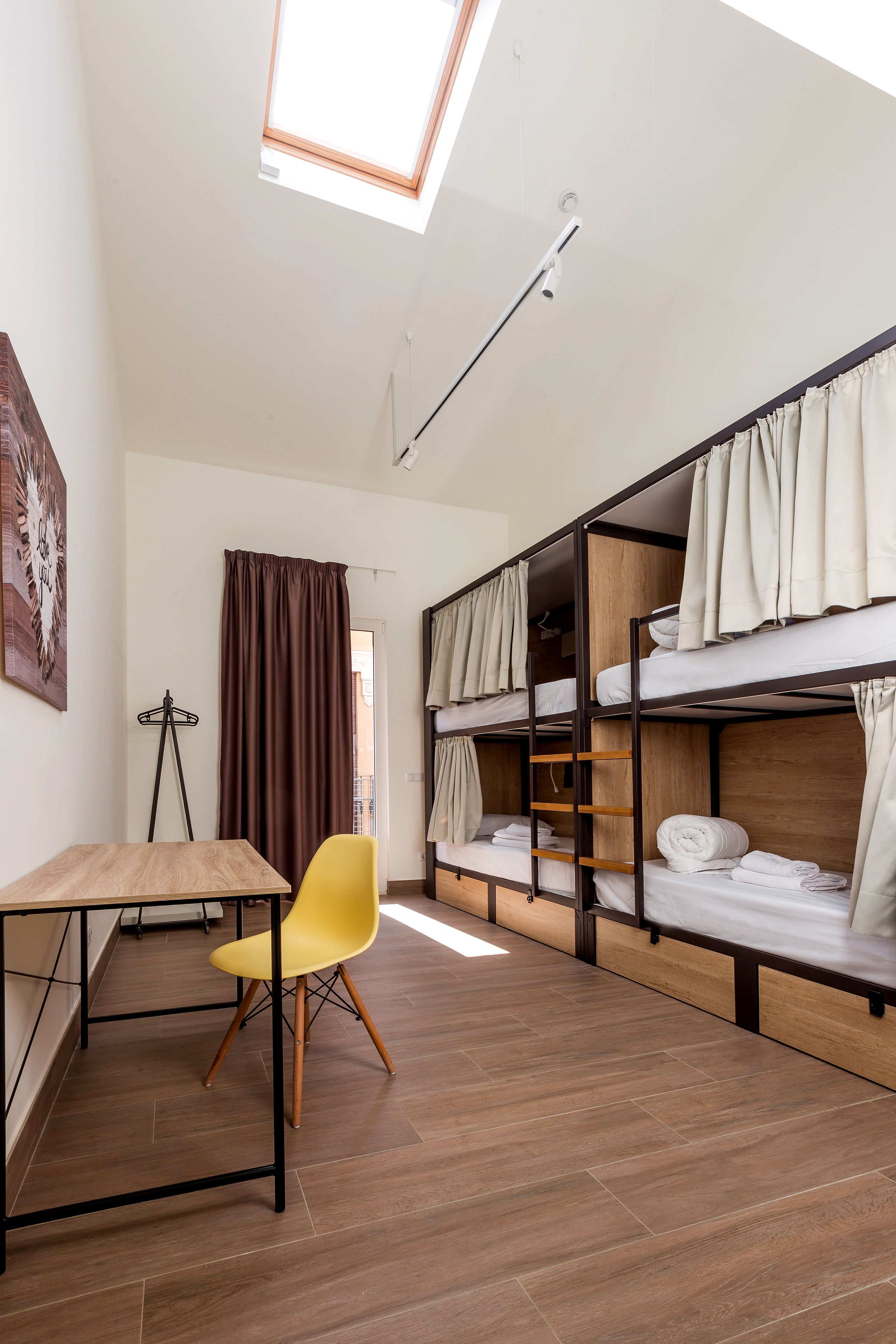Une chambre de dortoir avec des lits superposés, un bureau, une chaise et une lucarne.