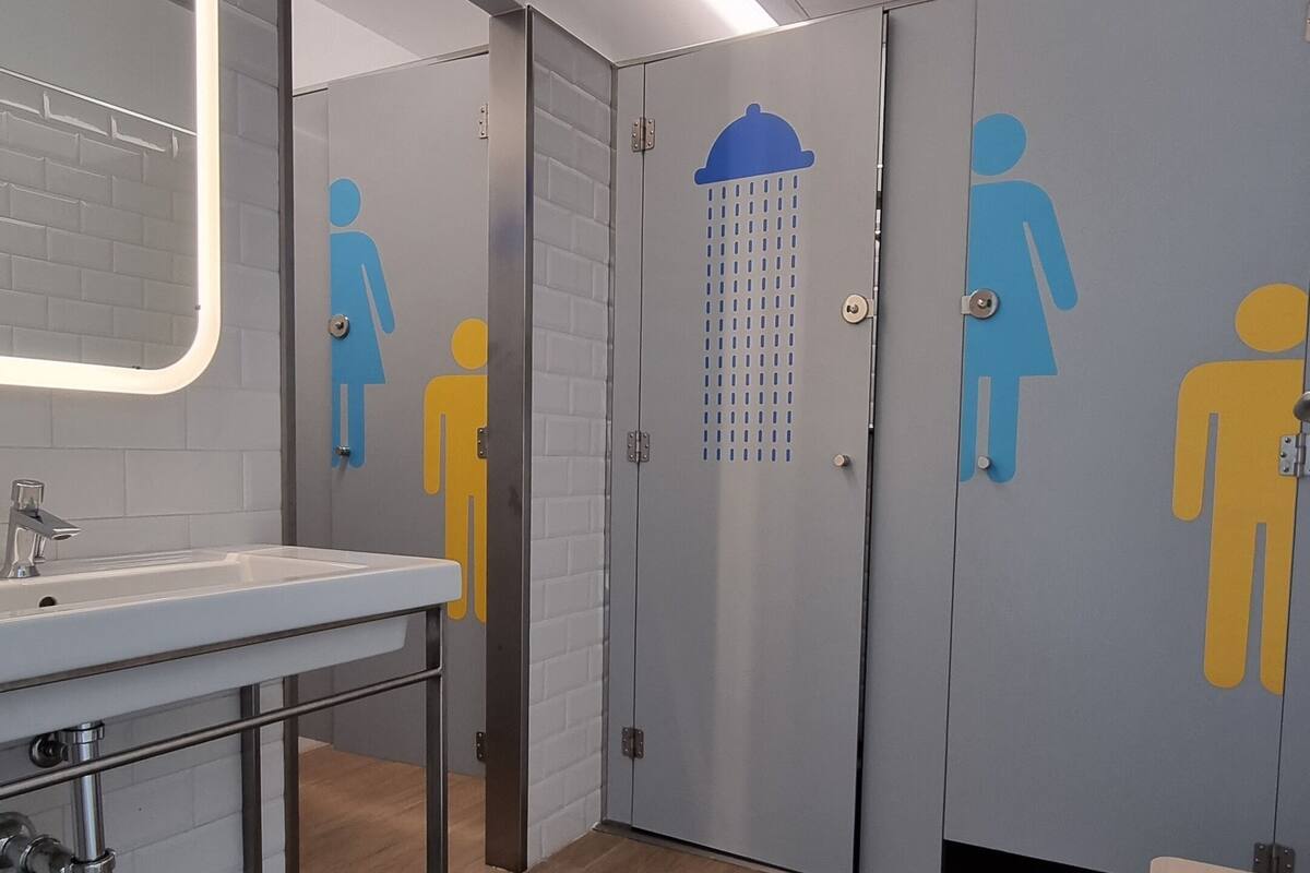 Een moderne badkamer met een wastafel, spiegel en douchecabines voorzien van gendersymbolen.
