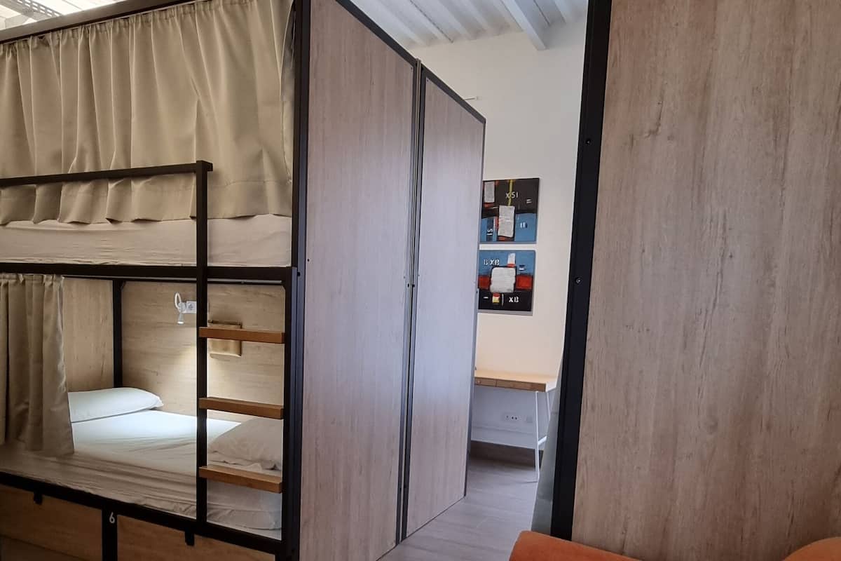 Een stapelbed met gordijn, een houten bureau en een oranje bank in een kamer met houten vloeren en een schuine kap.