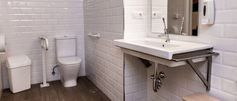 A modern bathroom with white subway tiles, a wooden floor, a white sink with a mirror, and a wooden bench.