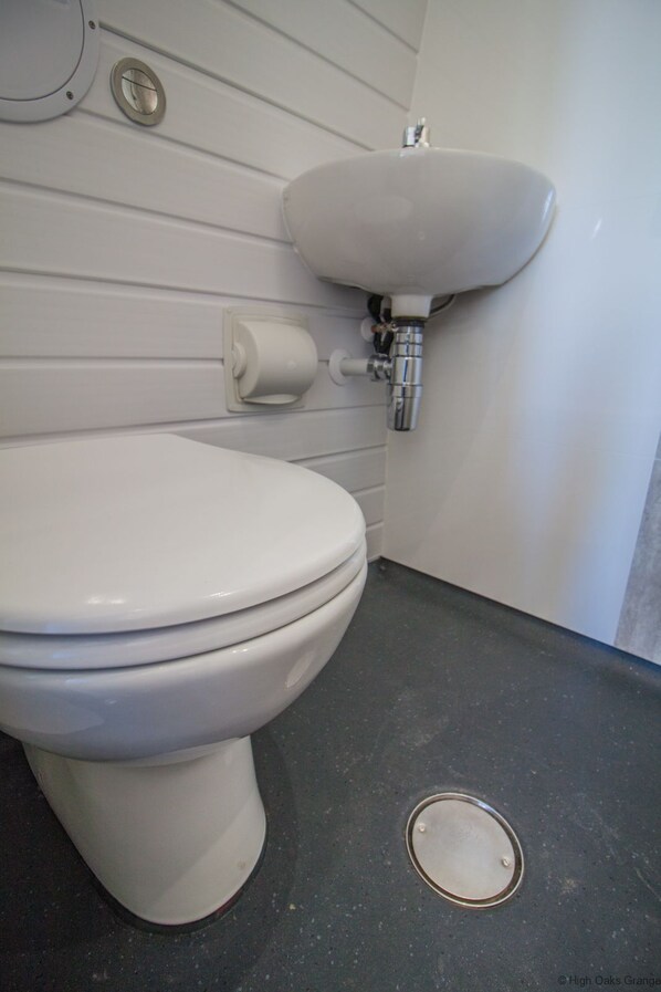 Des toilettes blanches dotées d’un siège-bidet, un lavabo et un porte-rouleau de papier toilette, le tout posé sur un sol gris.