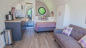 A compact bedroom with a bed, a sofa, a small kitchenette, and a circular window. - Bluebell Glamping Pod - sleeps 2 | Gold Award winning (Pickering)
